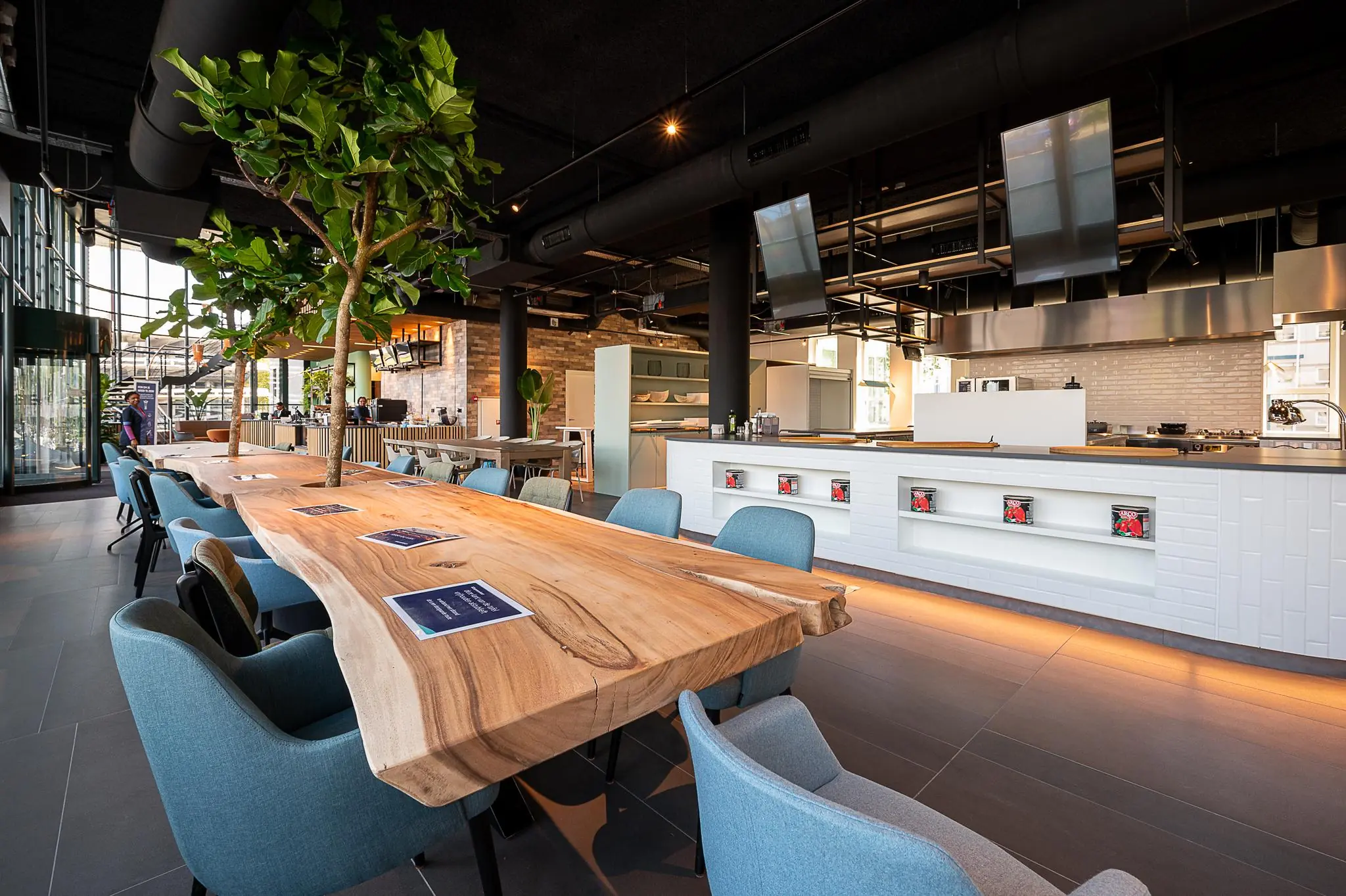 Moderne, open keuken met een lange houten tafel, blauwkleurige stoelen en groene binnenplanten aan de Watermanweg.