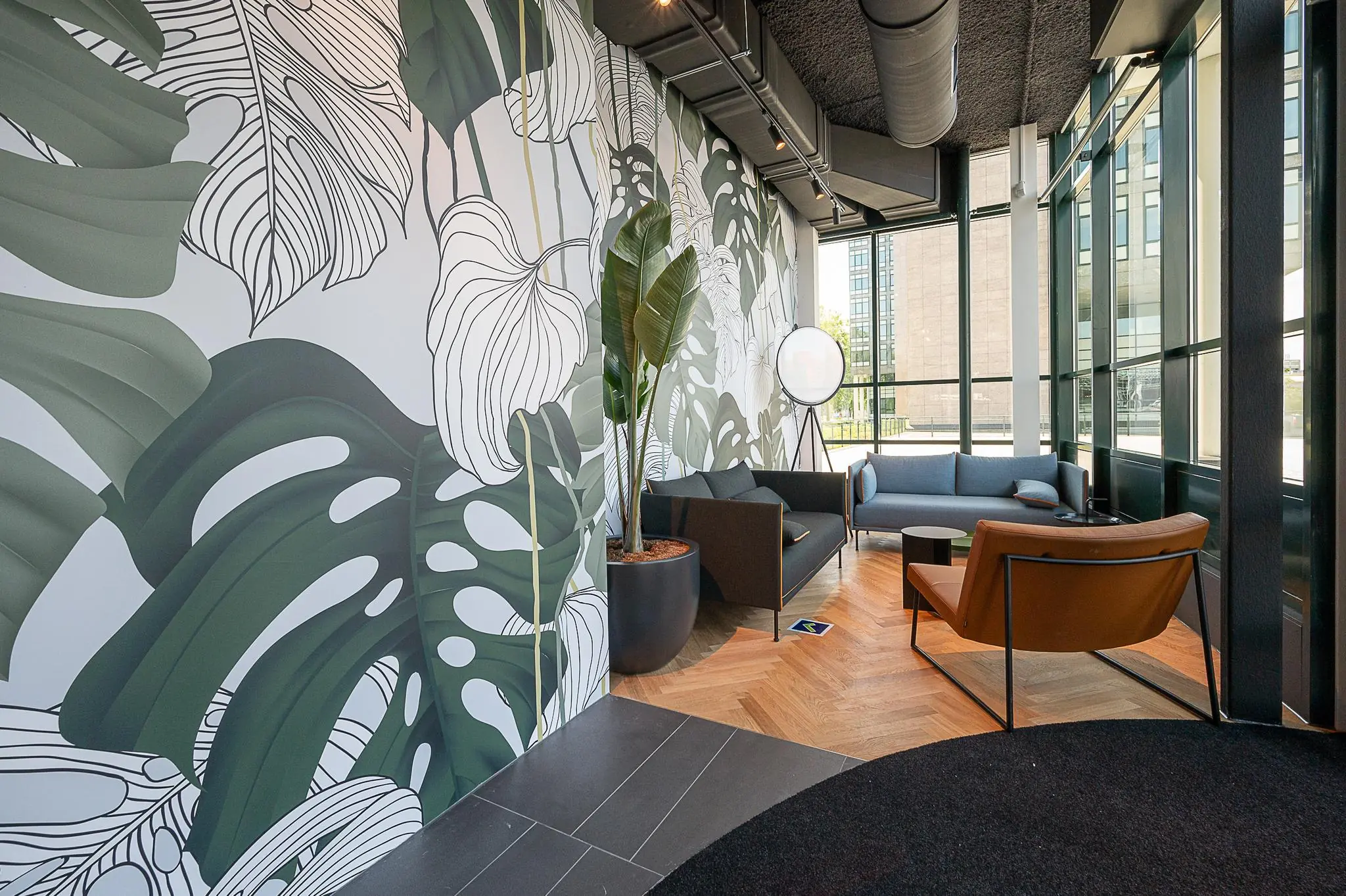 Moderne wachtruimte aan de Watermanweg met grote ramen, tropisch plantenbehang en stijlvolle zitmeubels.