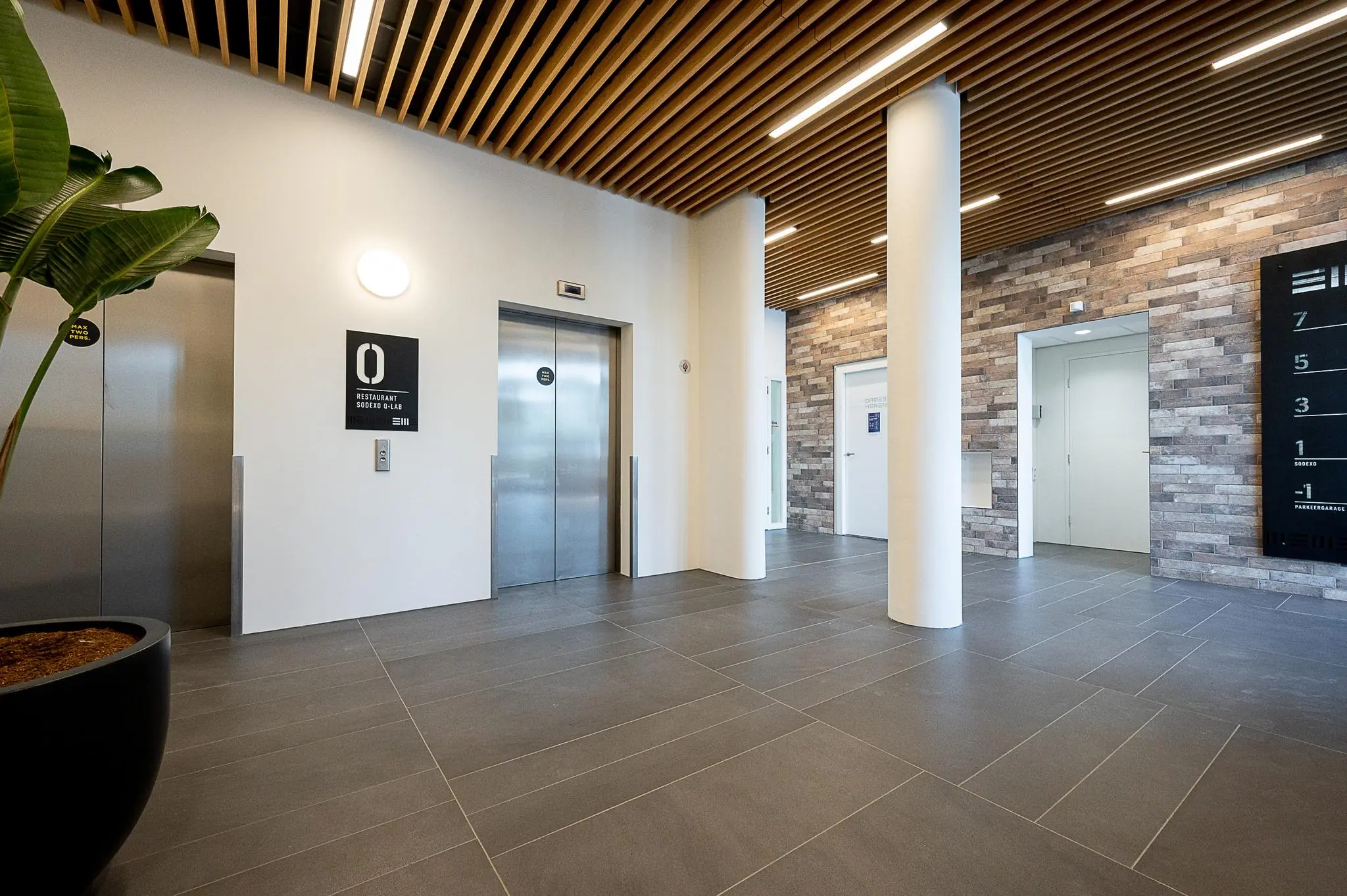 Moderne entreehal van een kantoorgebouw aan de Watermanweg met liften, houten plafond en stenen wand.