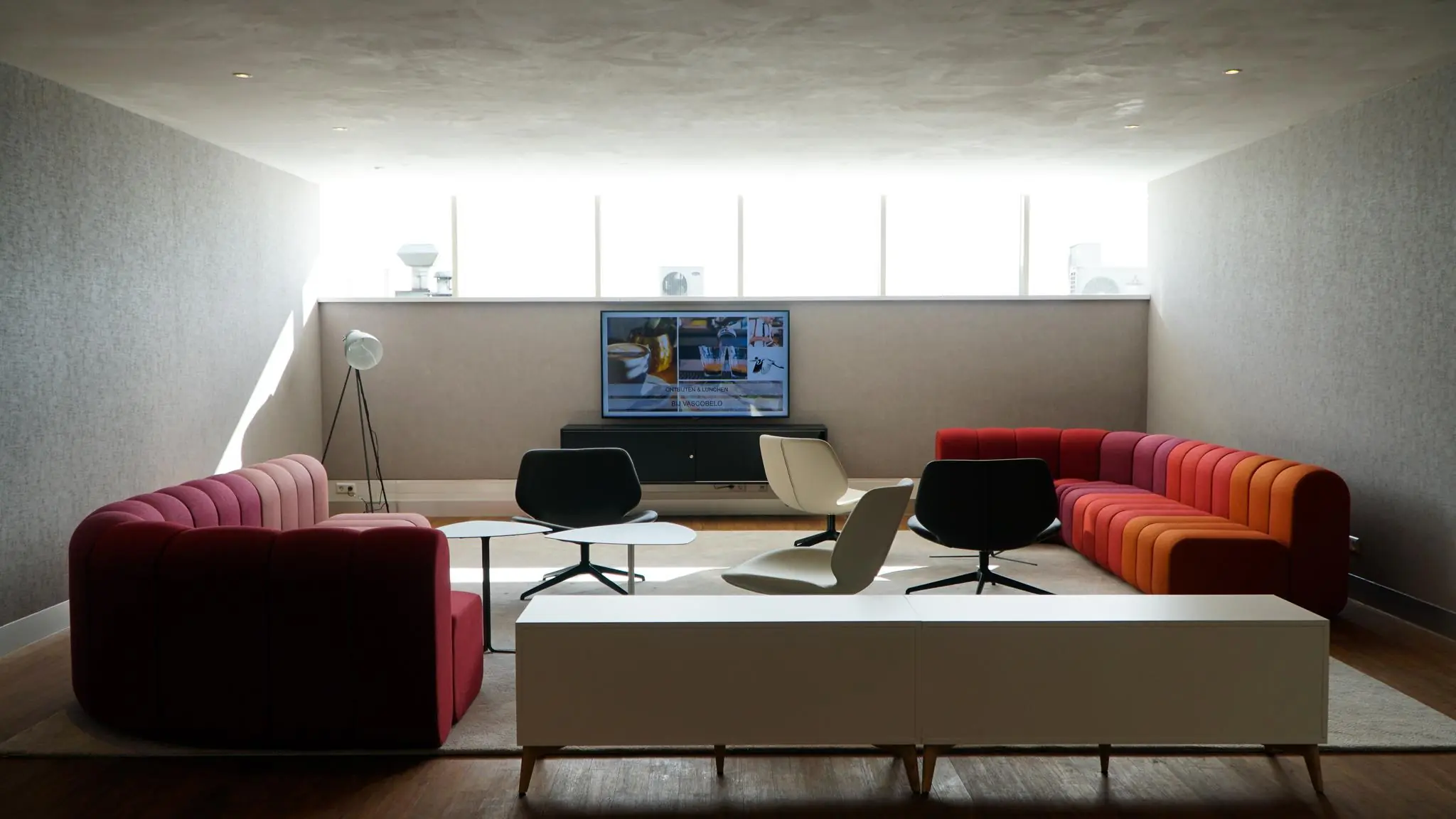 Moderne loungehoek met kleurrijke modulaire bank, designstoelen en een tv aan de muur bij Bisonspoor.