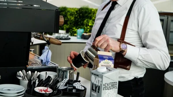 Barista schenkt melk in een koffiebeker naast een espressomachine.
