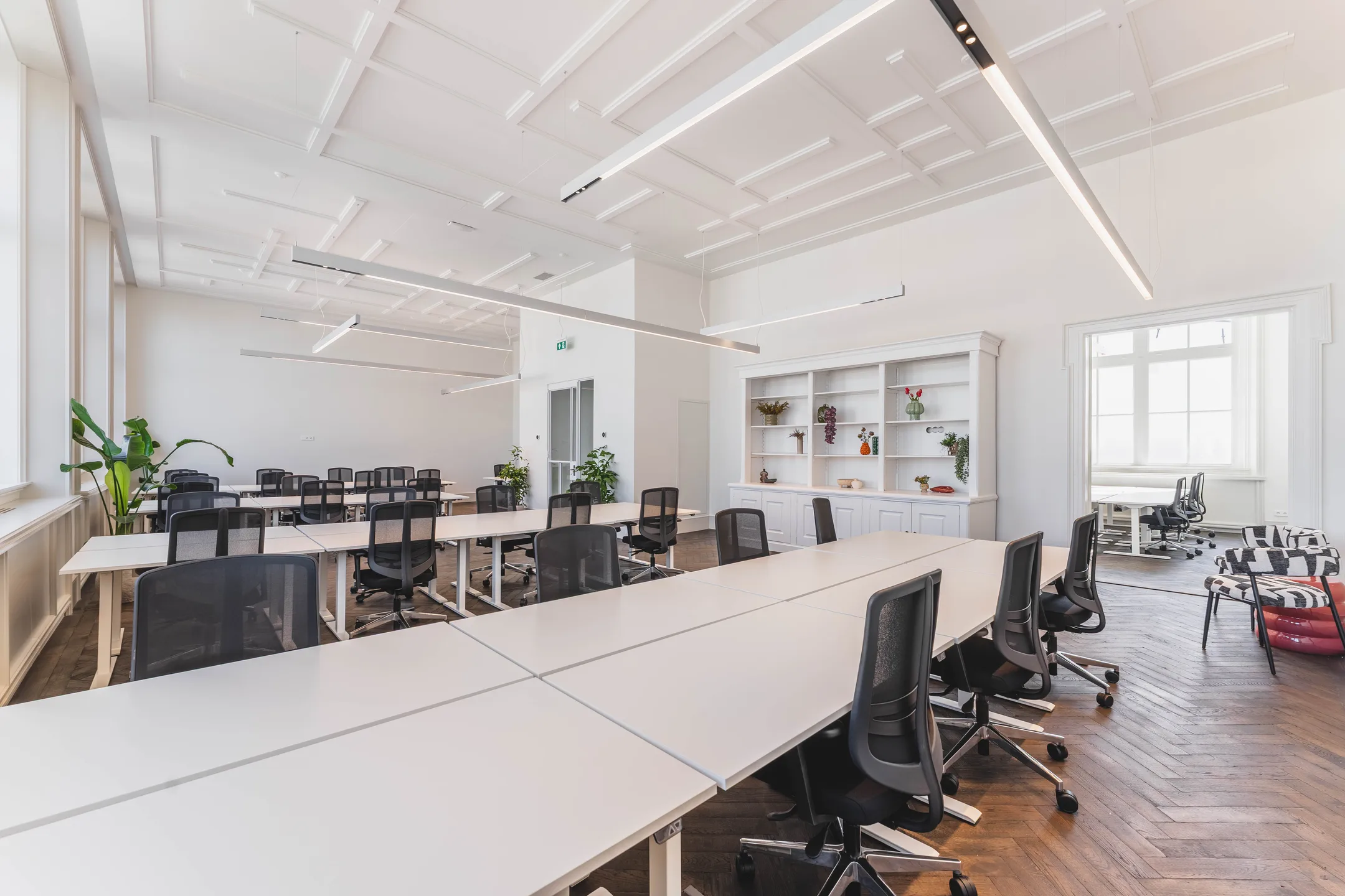Een moderne, ruime kantoorruimte met lange tafels, ergonomische bureaustoelen en planten.