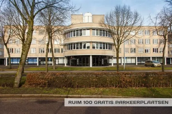 Vooraanzicht van een kantoorpand aan de Huizermaatweg met bomen en een bord met de tekst "Ruim 100 gratis parkeerplaatsen".