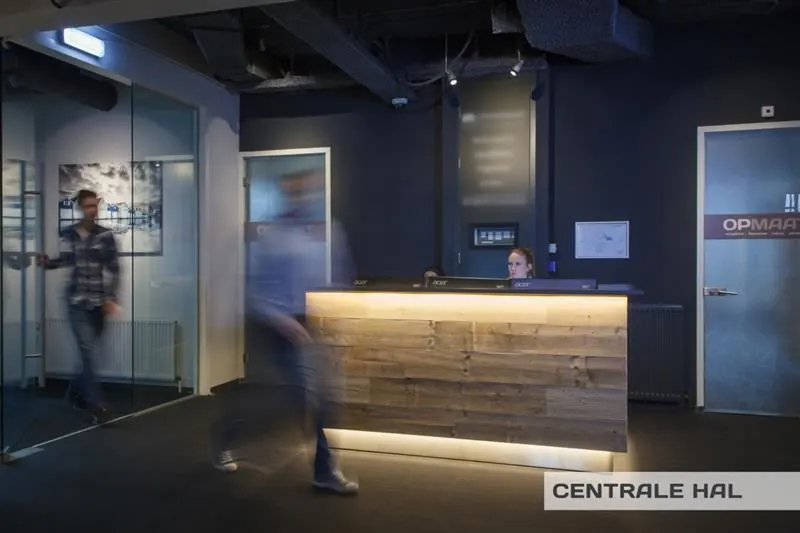 Receptiebalie in de centrale hal van een kantoor aan de Huizermaatweg, met mensen die langs lopen.