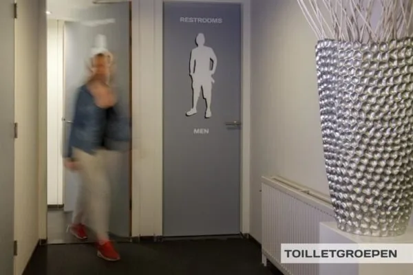 Gang met deuropeningen naar herentoilet en een persoon die voorbijloopt in een kantooromgeving aan de Huizermaatweg.