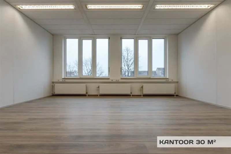 Leeg kantoor van 30 m² met houten vloer, witte wanden en grote ramen aan de Huizermaatweg.