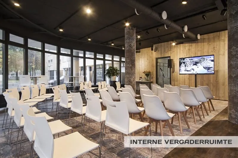 Moderne vergaderruimte met witte stoelen, een groot scherm en houten wandbekleding aan de Huizermaatweg.