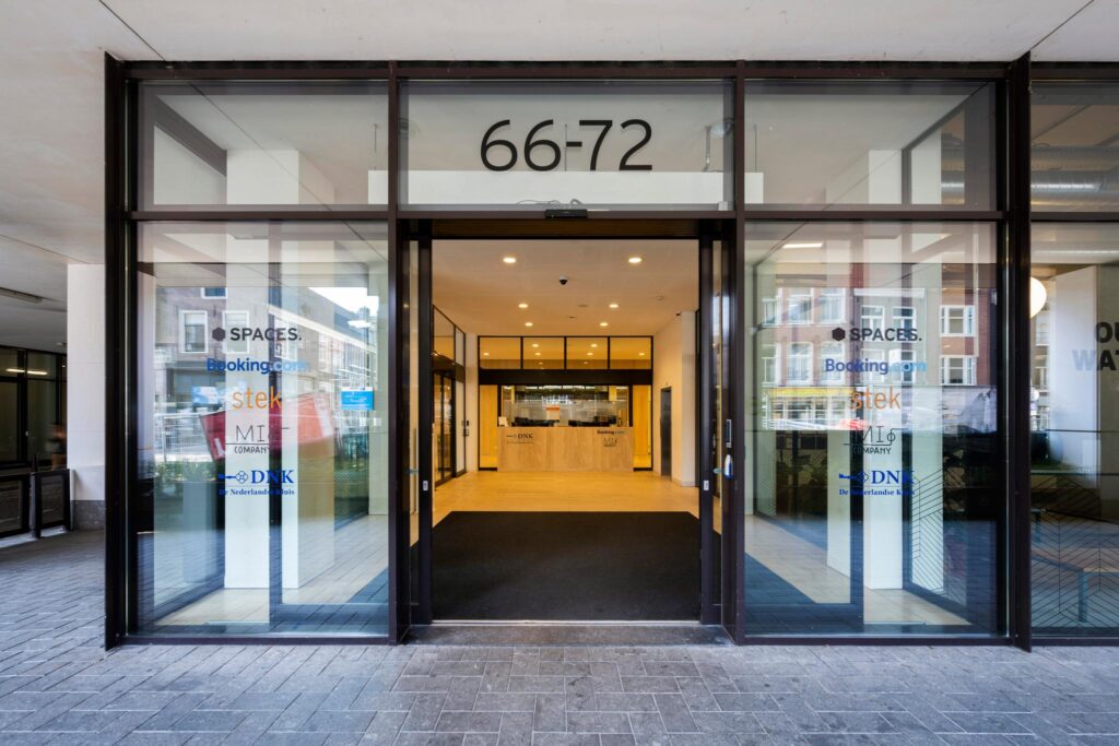 Glazen entree van het kantoorgebouw aan de Vijzelstraat 66-72 in Amsterdam met bedrijfsnamen op de ruiten.