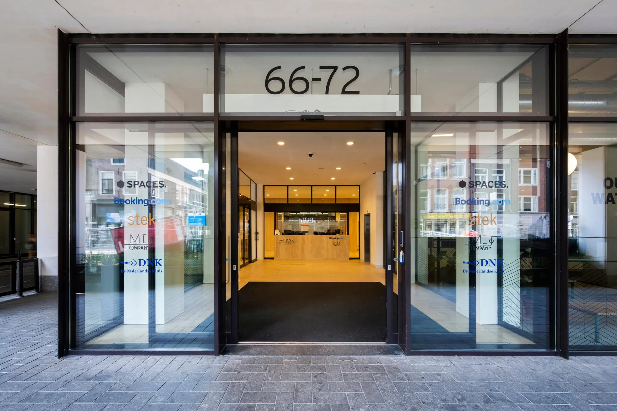 Glazen entree van het kantoorgebouw aan de Vijzelstraat 66-72 in Amsterdam met bedrijfsnamen op de ruiten.