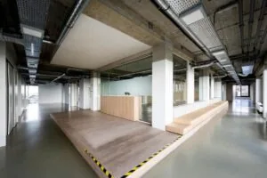 Moderne kantoorruimte aan de Vijzelstraat met een verhoogd houten platform, glazen wanden en een lange zitbank.