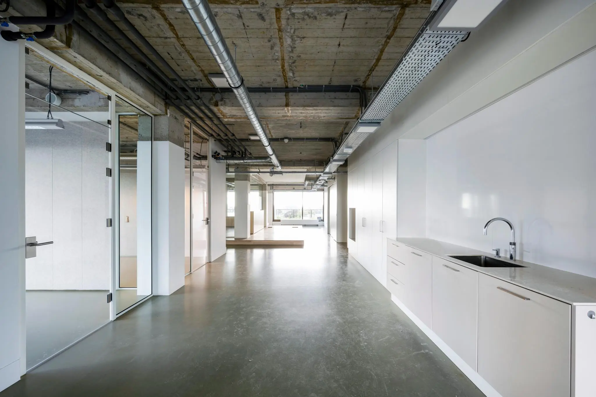 Modern industrieel kantoorinterieur aan de Vijzelstraat met een open ruimte, glazen wanden en een kitchenette.