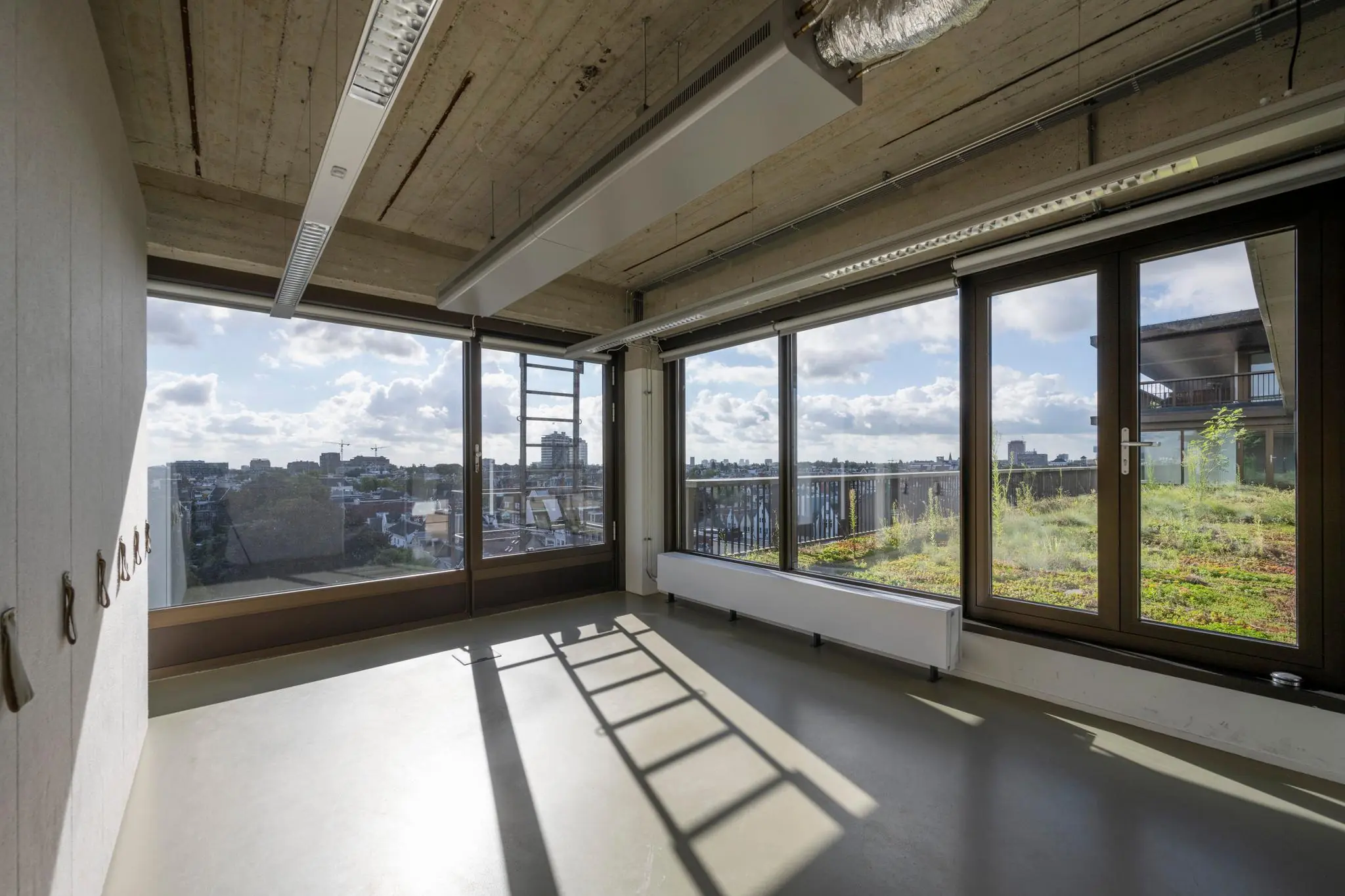 Licht en modern kantoorinterieur aan de Vijzelstraat met grote ramen en uitzicht op een groen dak en de stad.