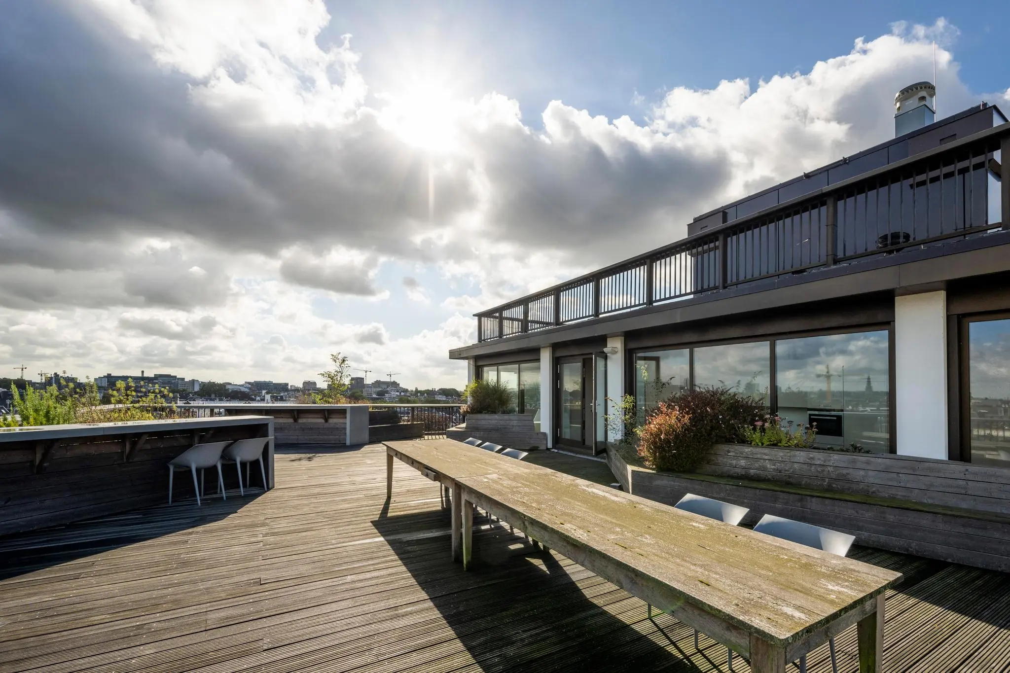 Dakterras aan de Vijzelstraat met houten zitgedeelte, plantenbakken en uitzicht op de stad onder een deels bewolkte hemel.