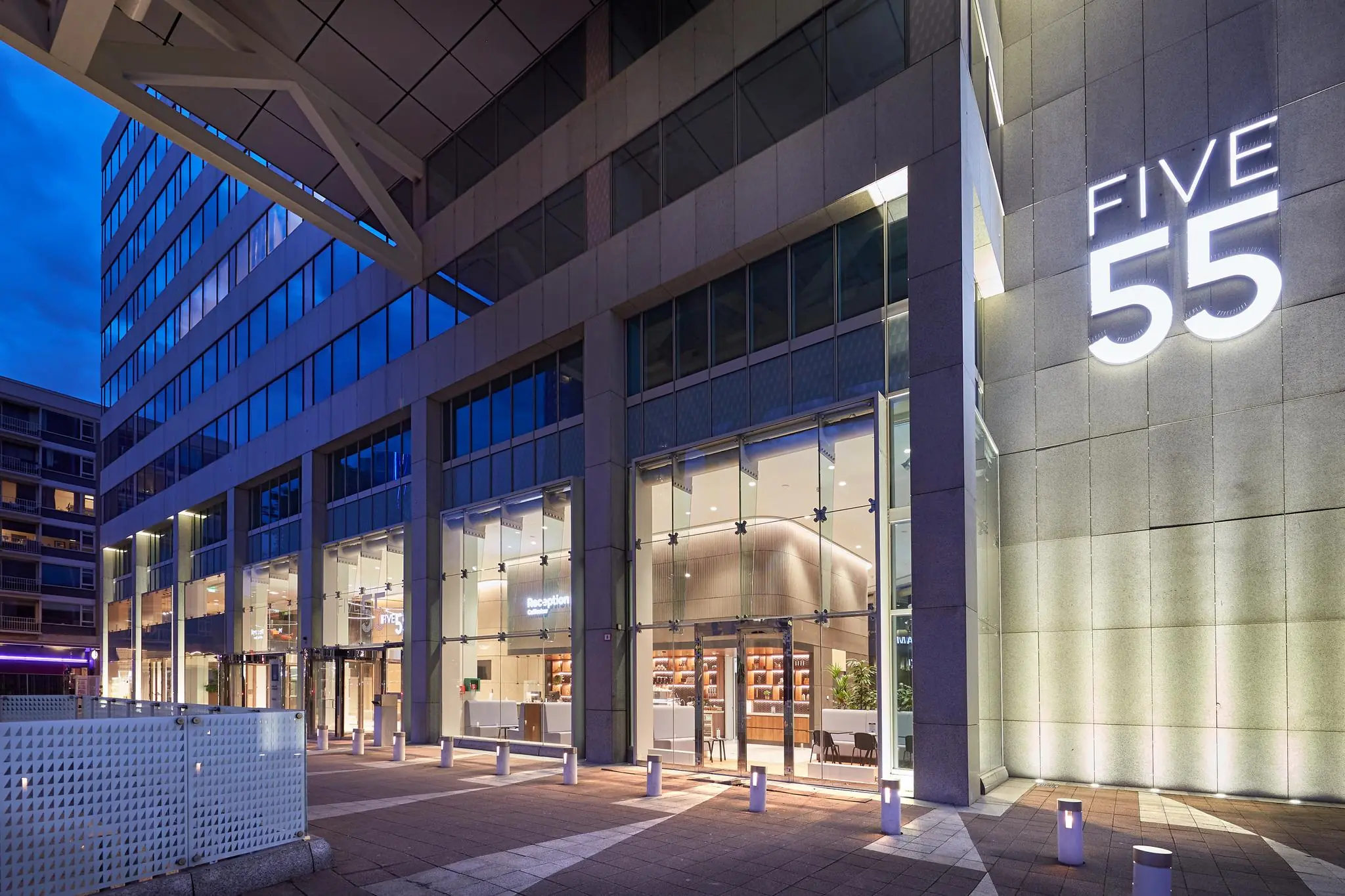 De modern verlichte entree van kantoorgebouw Five55 aan de Blaak in Rotterdam bij schemering.