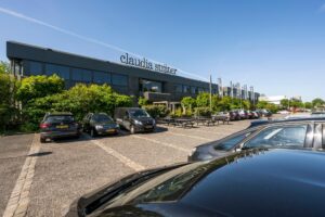 Vooraanzicht van het kantoorpand van Claudia Sträter met parkeerterrein en geparkeerde auto's.