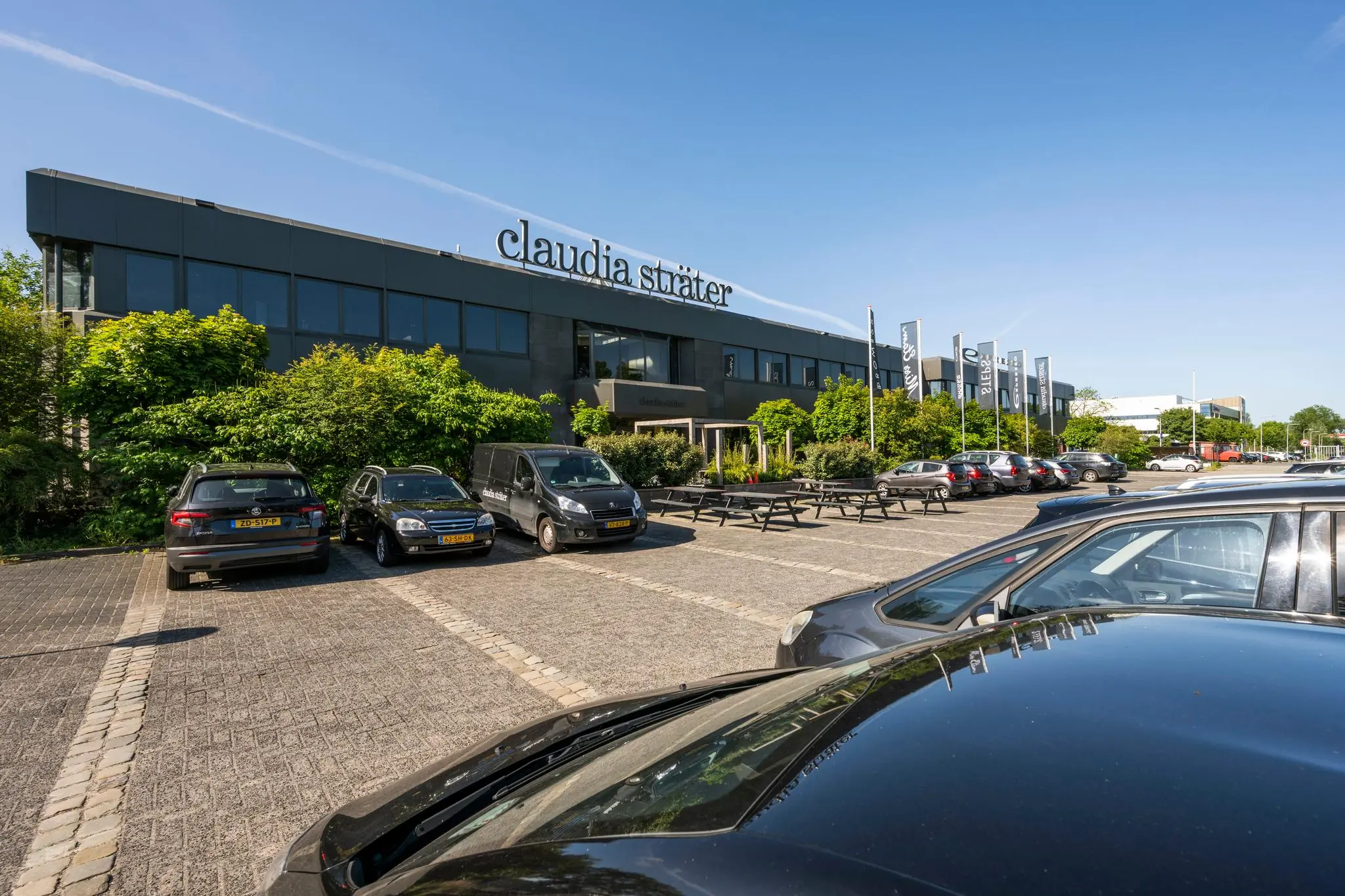 Vooraanzicht van het kantoorpand van Claudia Sträter met parkeerterrein en geparkeerde auto's.