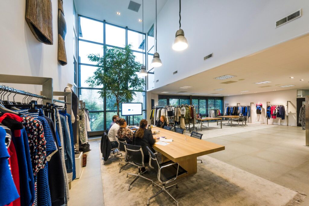 Moderne showroom met kledingrekken, een grote houten vergadertafel en mensen in bespreking bij Stammerhove.