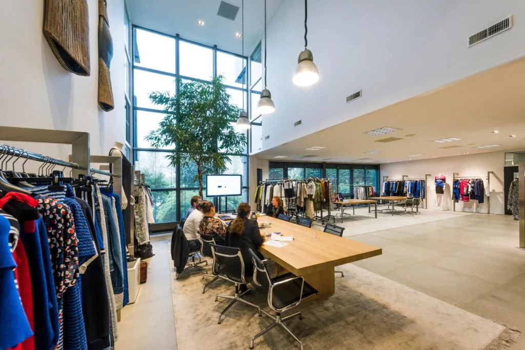 Moderne showroom met kledingrekken, een grote houten vergadertafel en mensen in bespreking bij Stammerhove.