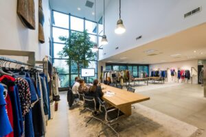 Moderne showroom met kledingrekken, een grote houten vergadertafel en mensen in bespreking bij Stammerhove.