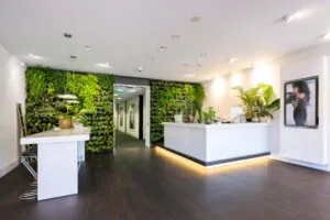 Moderne receptieruimte met witte balie, groene plantenwand en stijlvolle verlichting bij Stammerhove.