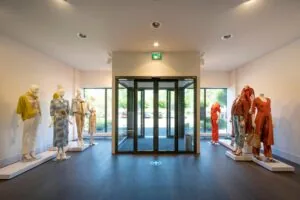 Entree van modewinkel Stammerhove met etalagepoppen in zomerse kleding aan weerszijden van een glazen draaideur.