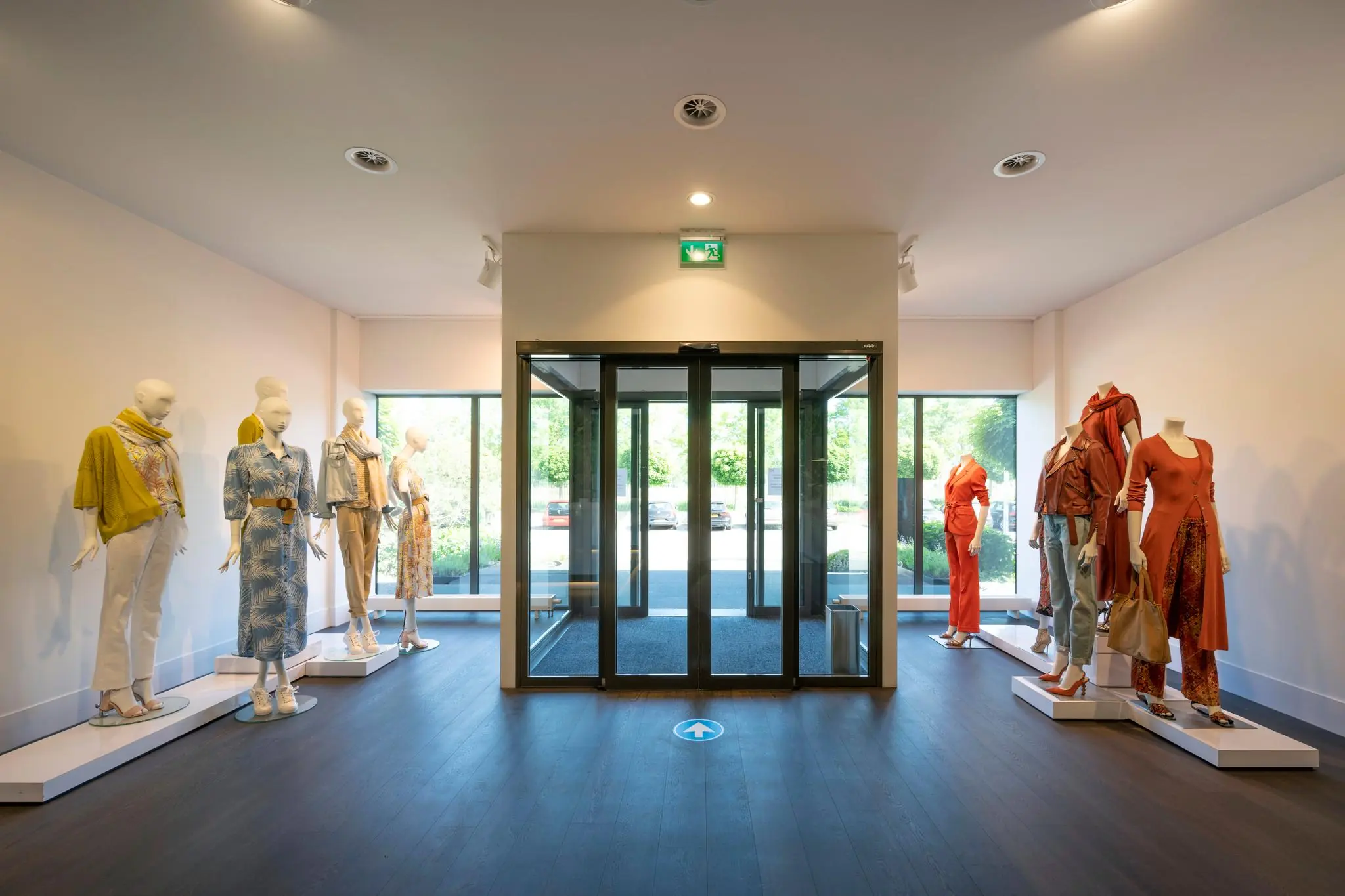 Entree van modewinkel Stammerhove met etalagepoppen in zomerse kleding aan weerszijden van een glazen draaideur.