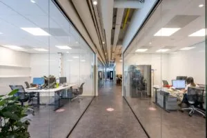 Gang met glazen wanden in een modern kantoorpand aan de Stammerhove met werkplekken aan weerszijden.