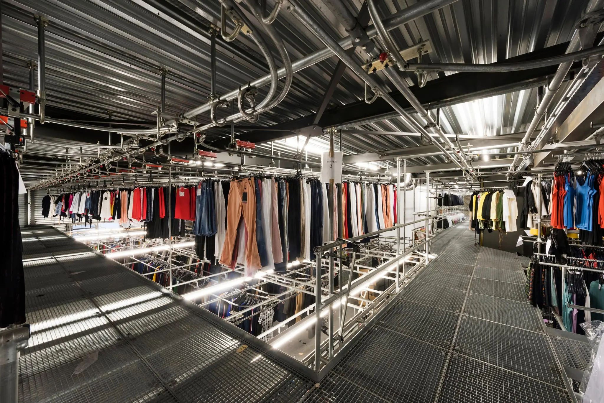 Overzicht van een geautomatiseerd kledingdistributiesysteem met hangende kledingstukken in een magazijn.