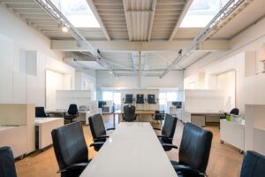 Modern, licht kantoorinterieur met lege bureaus, zwarte bureaustoelen en een lange vergadertafel.