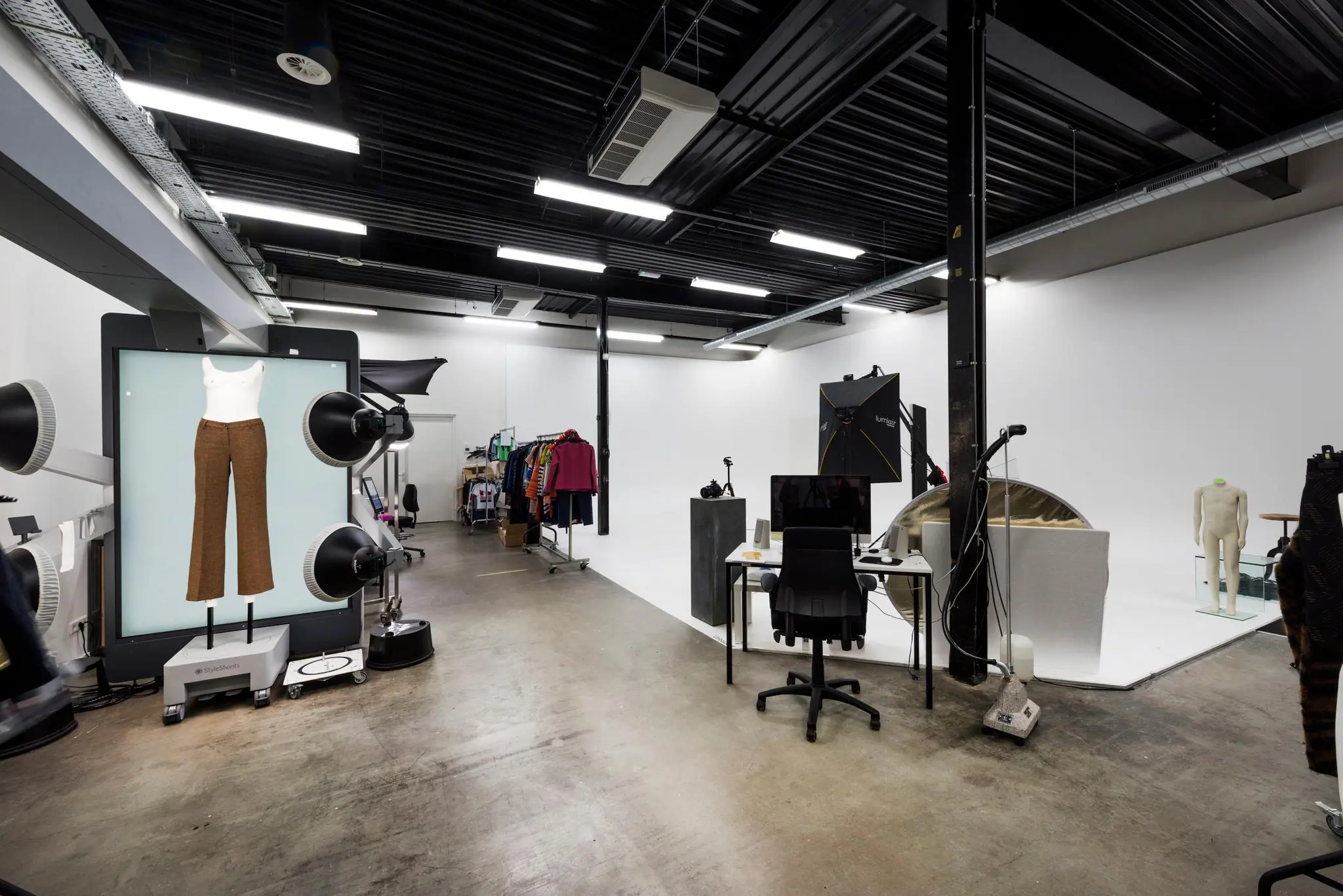 Professionele fotostudio met kledingrekken, verlichting en apparatuur voor modefotografie.