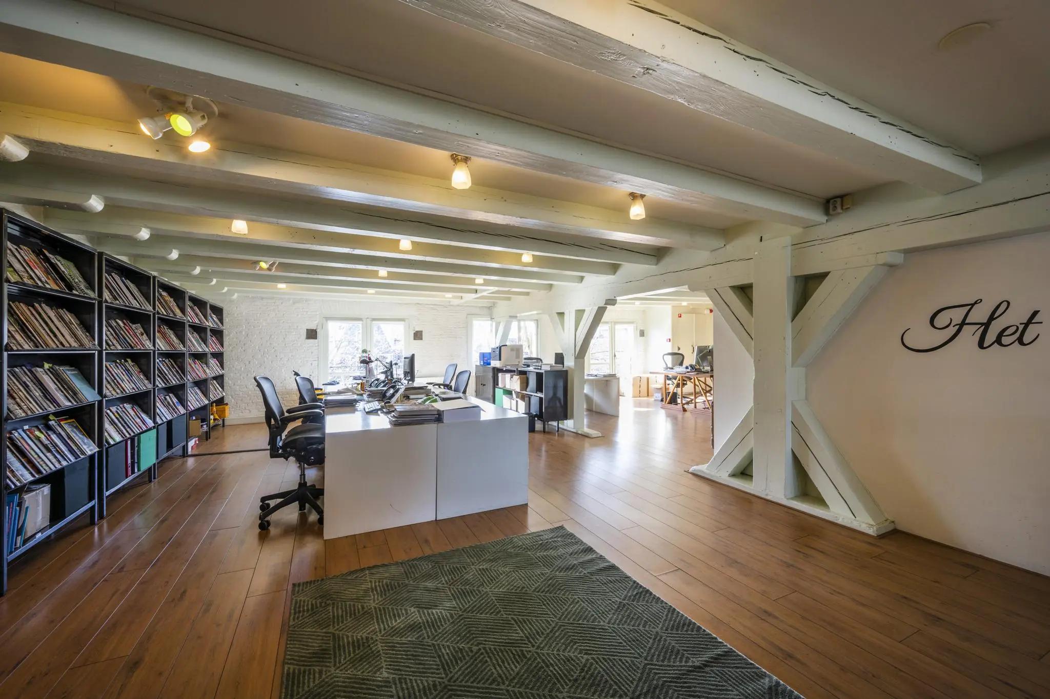 Modern open kantoor op de Leidsegracht met houten balkenplafond, bureaus, boekenkasten en daglicht.