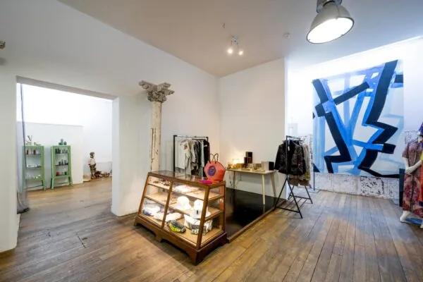 Boetiek aan de Leidsegracht met houten vloer, vintage vitrinekast, kunst aan de muur en kledingrekken met designerstukken.