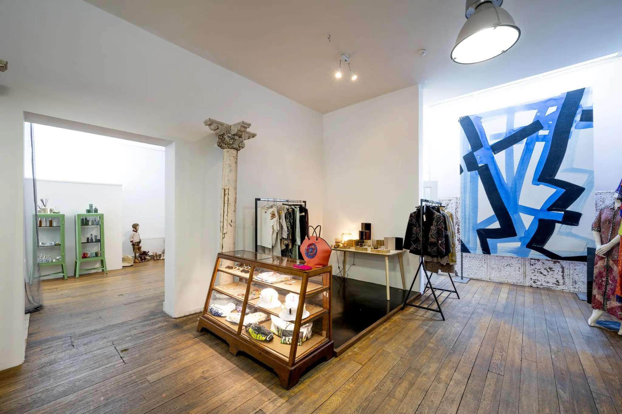 Boetiek aan de Leidsegracht met houten vloer, vintage vitrinekast, kunst aan de muur en kledingrekken met designerstukken.