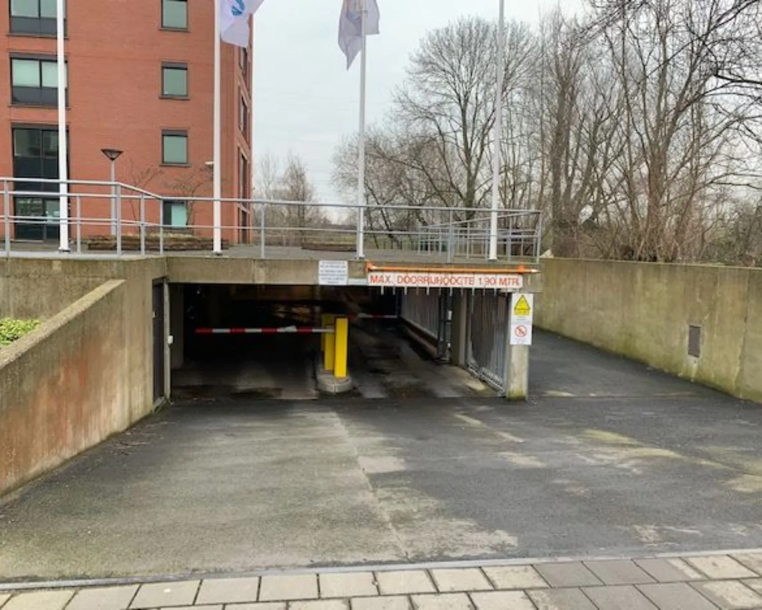 Ingang van een ondergrondse parkeergarage met een hoogtebeperking van 1,90 meter bij een rood bakstenen kantoorgebouw.