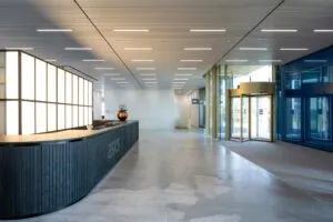 Moderne ontvangsthal van het ASICS-kantoor aan Taurusavenue met een ronde balie, glazen draaideur en strakke verlichting.