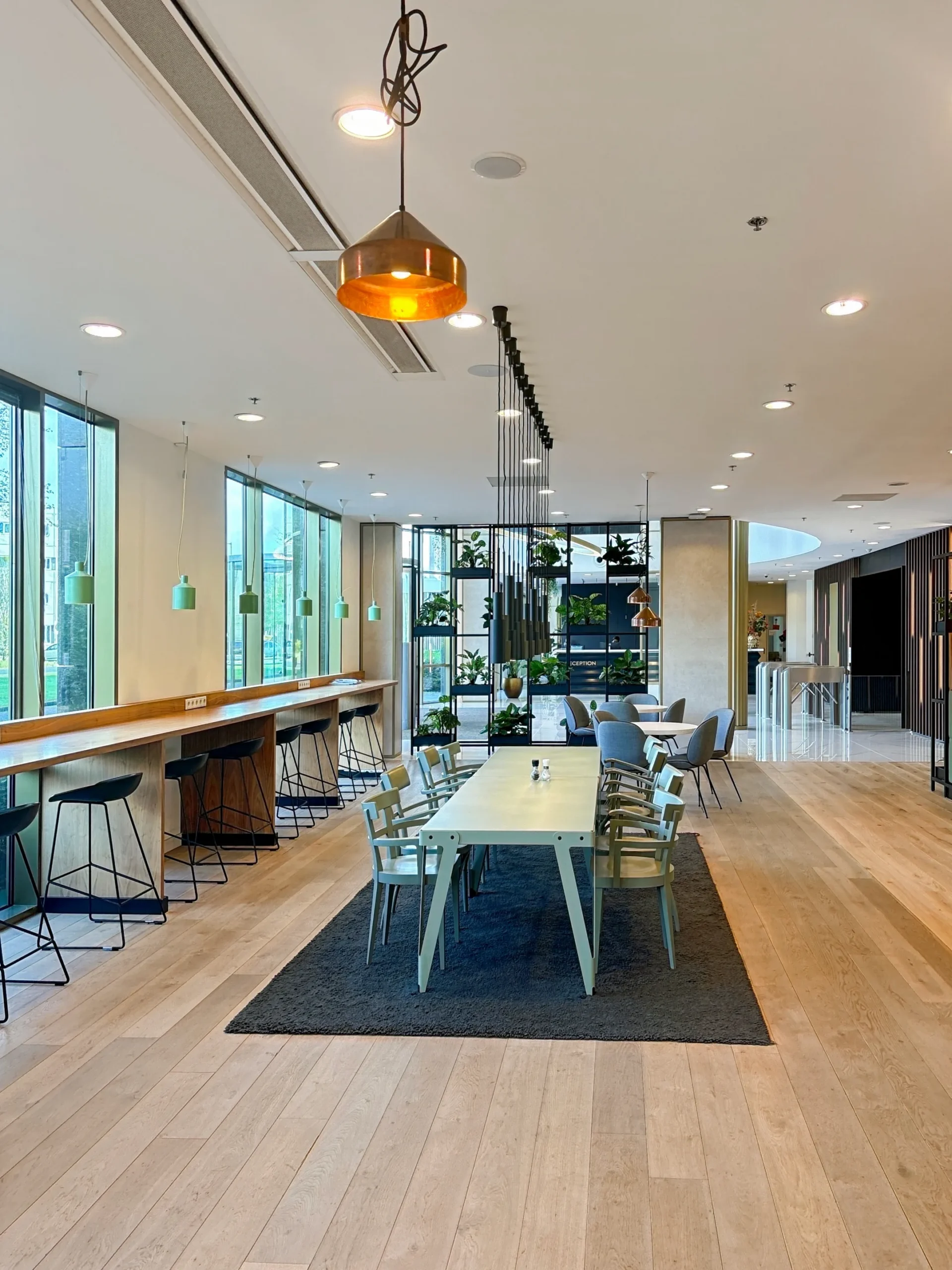 Moderne kantoorruimte met een lange tafel, eetkamerstoelen, hoge krukken bij de ramen en hangende verlichting.