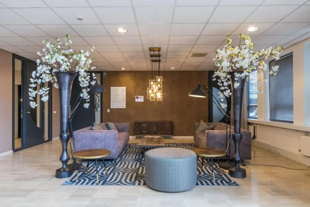 Moderne wachtruimte met paarse banken, grote bloemstukken en een geometrisch vloerkleed.