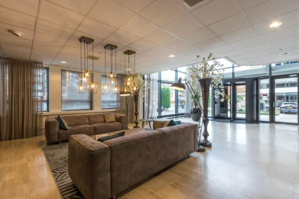Moderne en sfeervolle hotellobby met comfortabele banken, hanglampen en grote ramen die uitzicht bieden op de straat.