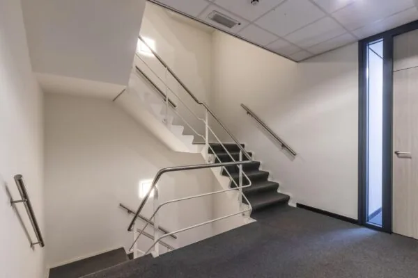 Trapportaal in een modern kantoorgebouw met grijze vloerbedekking en metalen leuningen.
