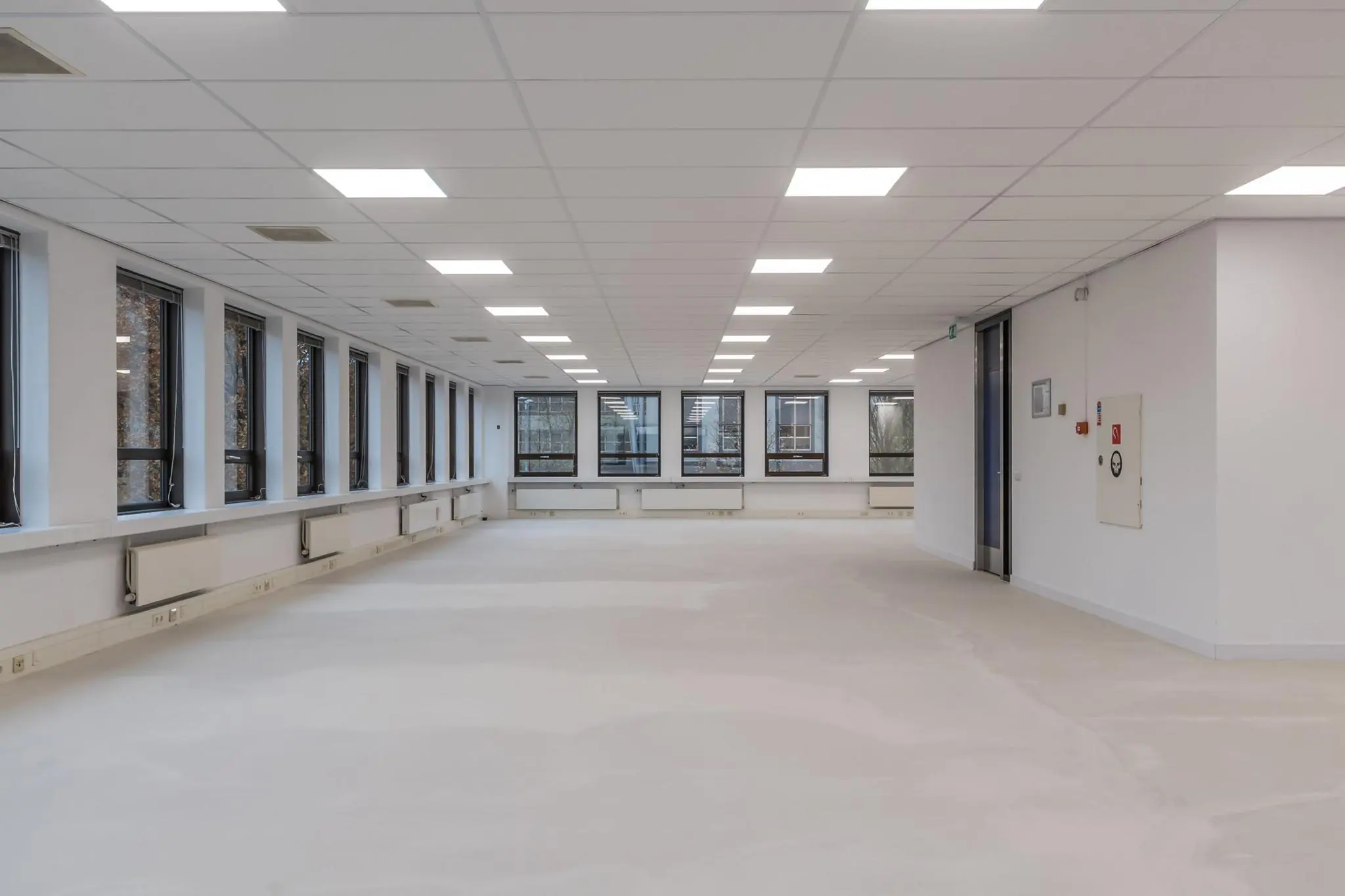 Lege, modern og verlichte kantoorruimte met grote ramen en systeemplafond.