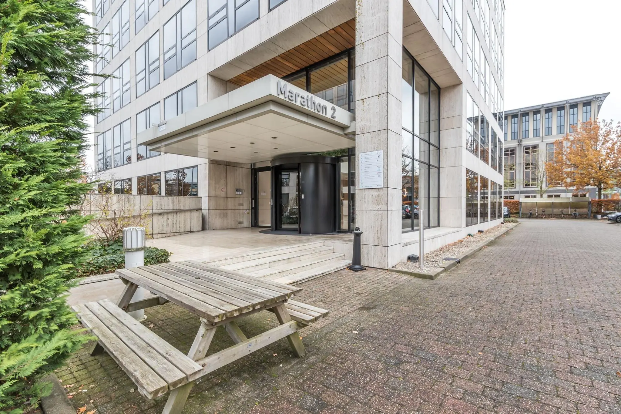 Ingang van kantoorgebouw Marathon 2 met een houten picknicktafel op de voorgrond.