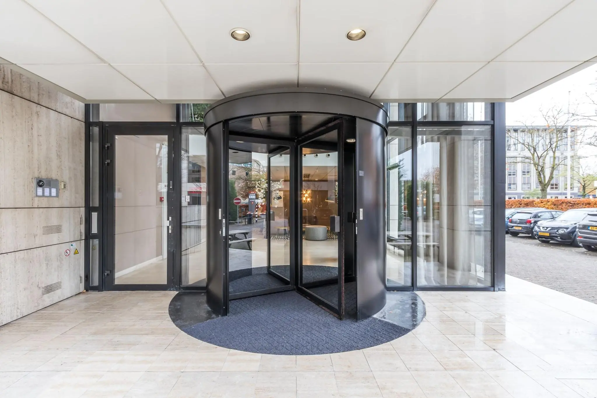Ingang van een modern kantoorgebouw met een glazen draaideur en marmeren vloer.