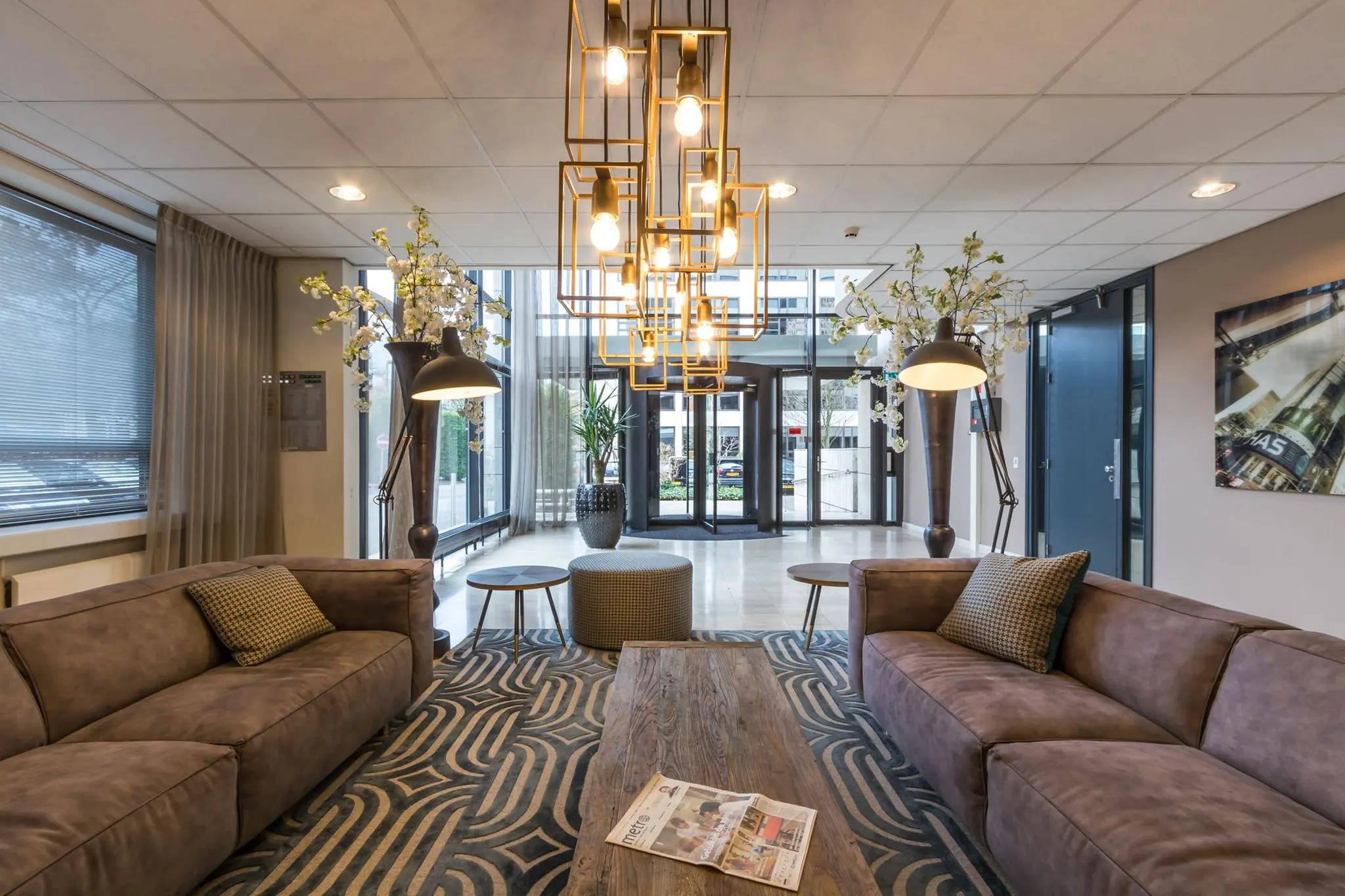 Modern ingerichte hotellobby met twee bruine banken, hanglampen, een houten salontafel en grote ramen aan de voorzijde.