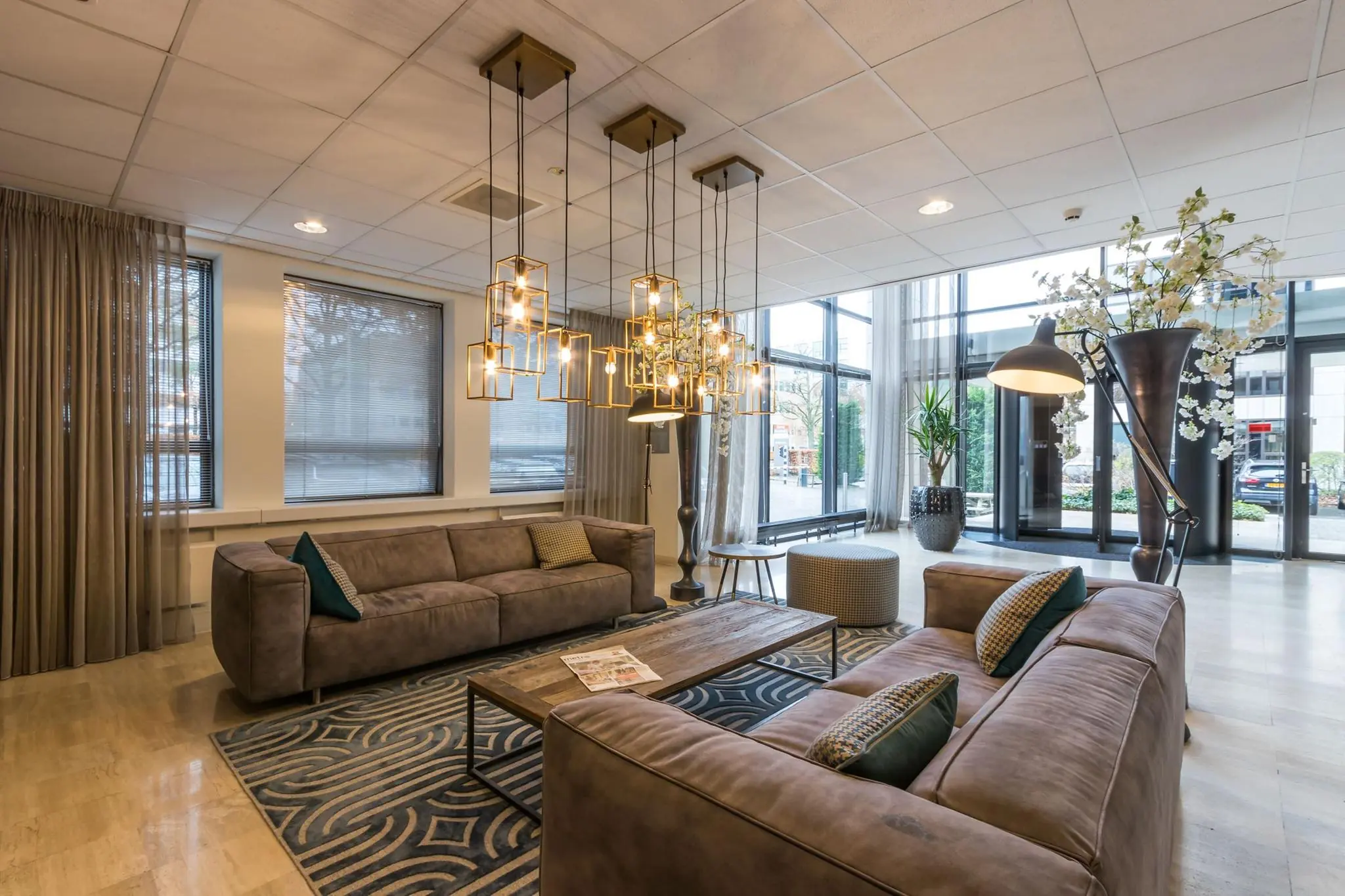 Moderne hotellobby met comfortabele banken, decoratieve verlichting en grote ramen die veel daglicht binnenlaten.