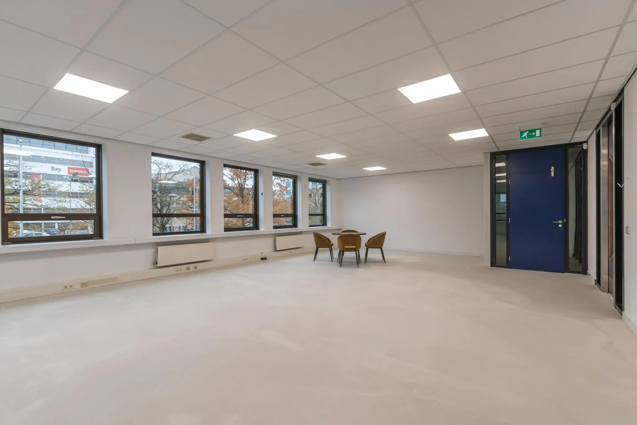 Leeg kantoorpand met vier stoelen en een ronde tafel bij het raam.