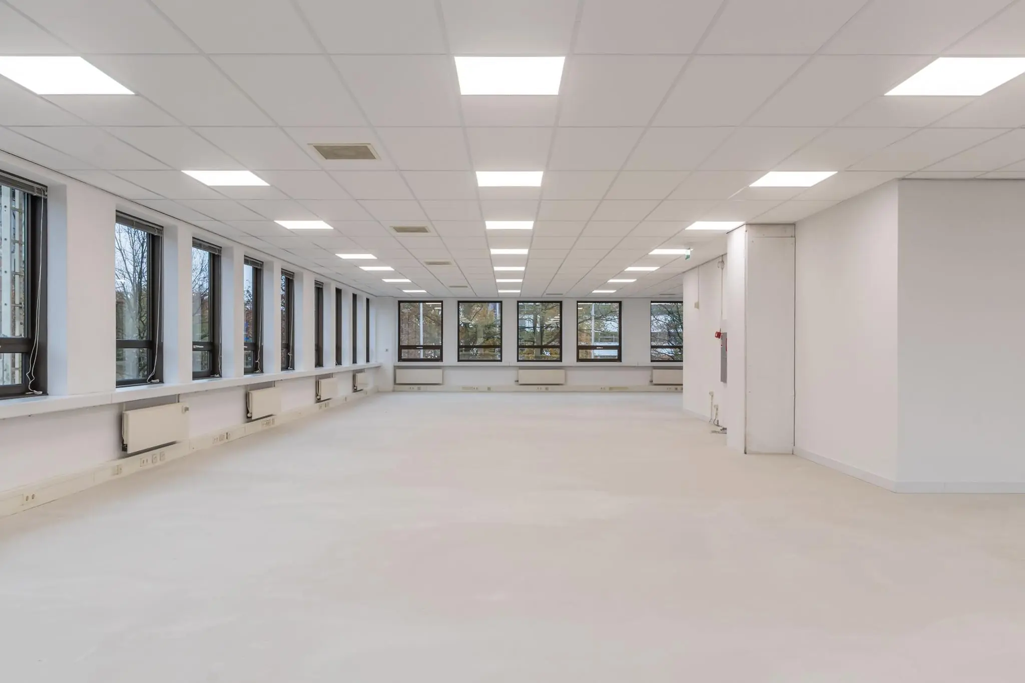 Lege, goed verlichte kantoorruimte met grote ramen en een systeemplafond.