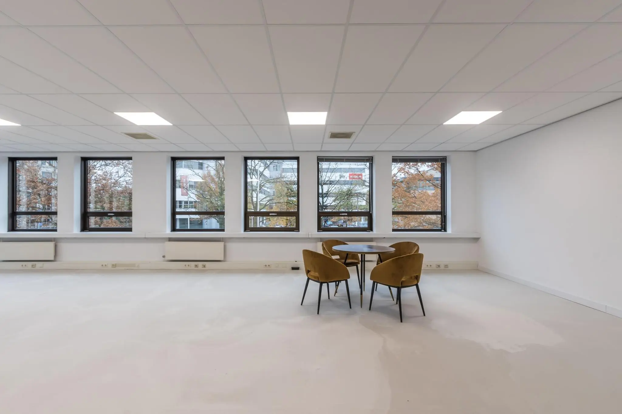 Lege kantoorruimte met vijf ramen en een ronde tafel met vier stoelen.