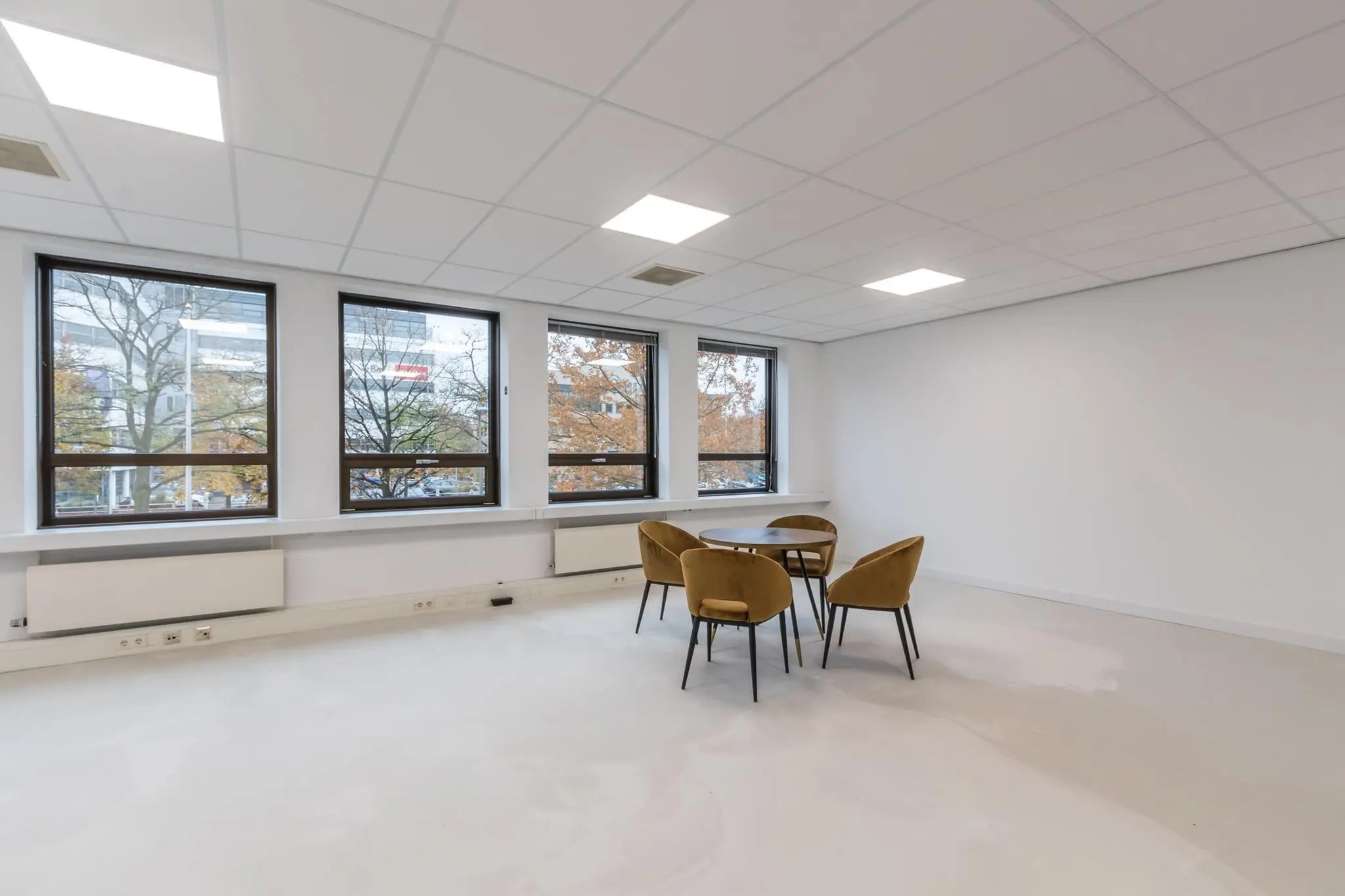 Lichte, minimalistisch ingerichte kantoorruimte met ronde tafel en vier stoelen bij grote ramen.