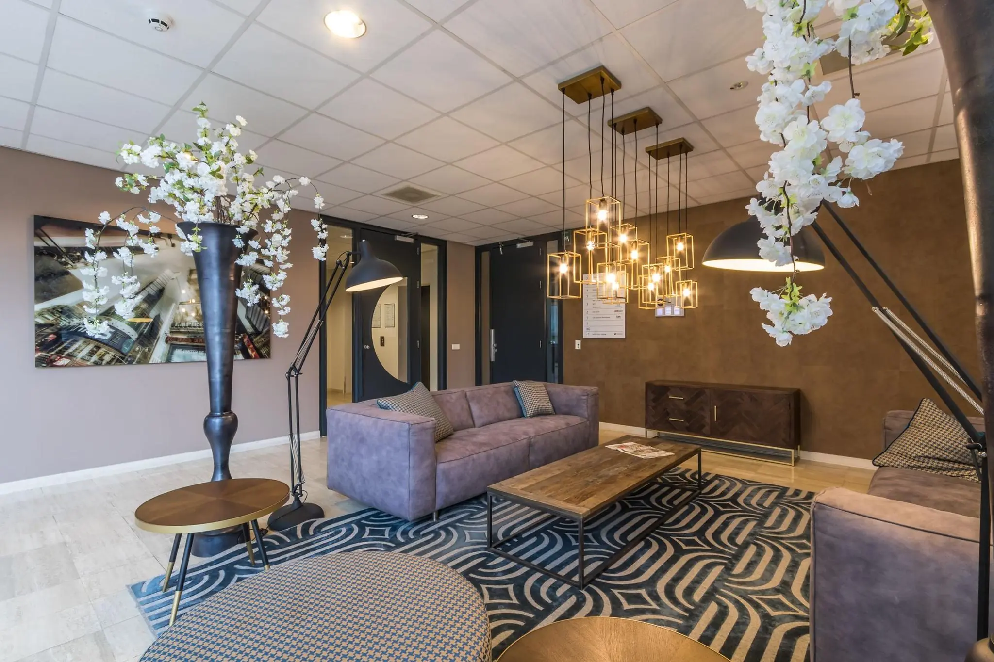 Moderne wachtruimte met paarse banken, houten accenten, hanglampen en decoratieve bloesemtakken.