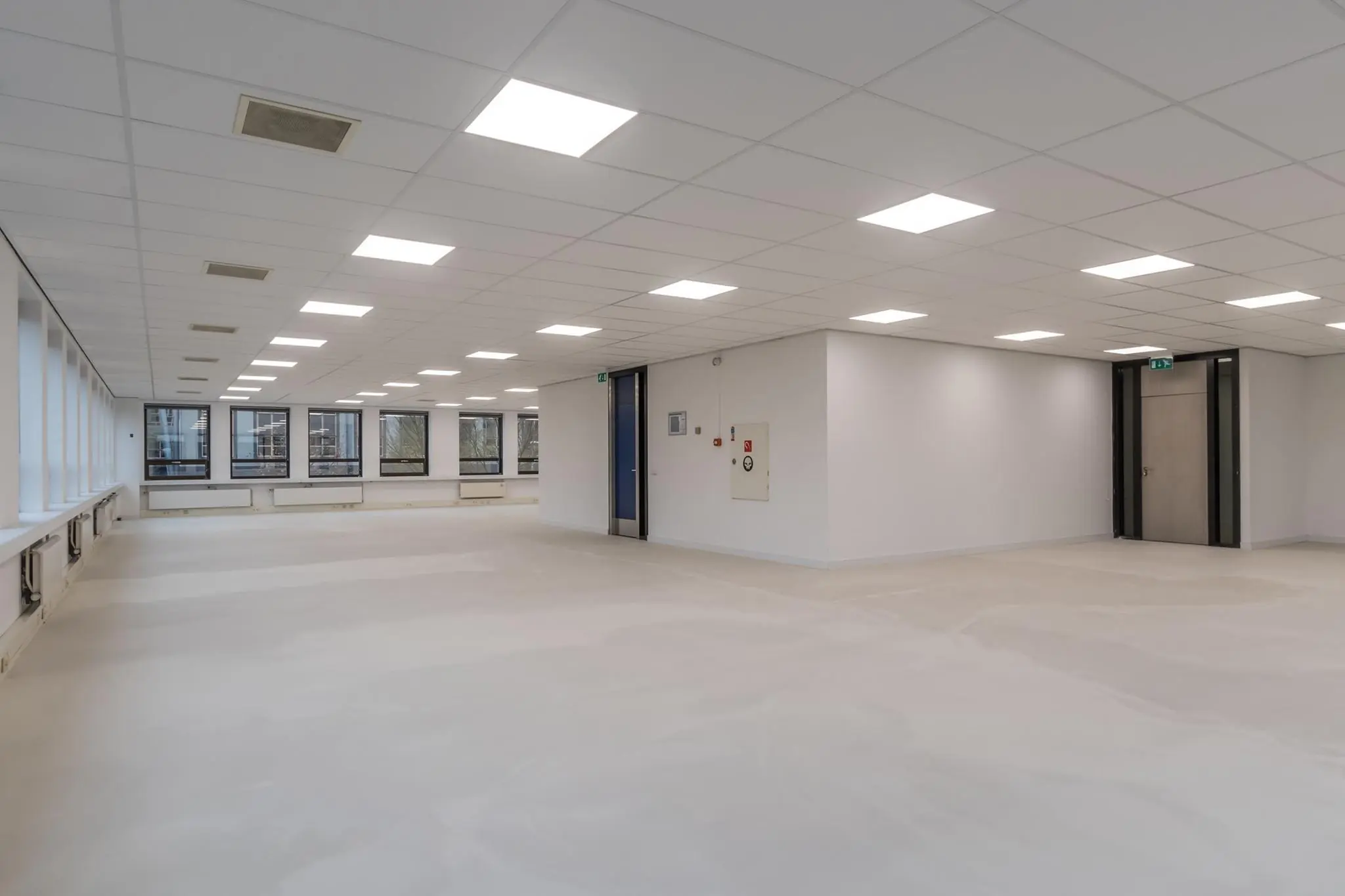 Lege, moderne kantoorruimte met systeemplafond, LED-verlichting en grote ramen.